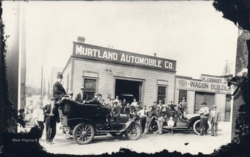 Exterior of Murtland Automobile Company; people and automobiles are in front; also includes storefront of "H.J. Domhoff, Wagon Builder."