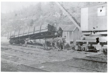 Crane and crew members putting a railroad car back on the track.