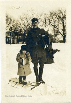 Candid portrait of Lt. Louis Bennett in uniform posing with a small child on a sled.