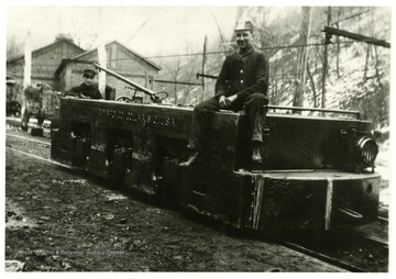 Two men riding on a electric locomotive. 