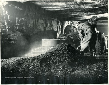 Two miners digging coal in mine.