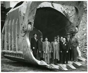 Group portrait of men standing in the bucket of a large shovel.