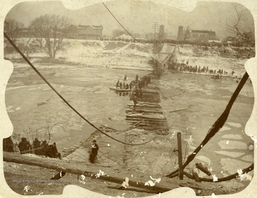 Crowds gather along the banks of the Elk River while people walk out on the fallen bridge to rescue people in the water.