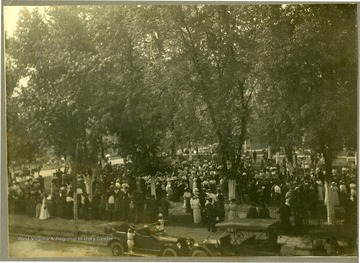 Large group of people gather together under trees in Charleston, W. Va. Location is possibly the old state capitol grounds.
