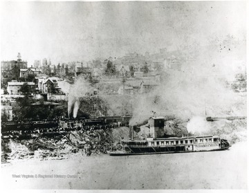 The Florence Belle pulling up to the edge of the river next to a train. 'At foot of Quincy St., showing Capt. Walker's House and Cal Arnett's home, one of the first modern homes in the city.' 
