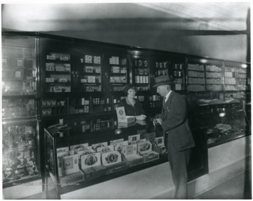 Interior view of C. G. Turner's Store in Grafton, W. Va.  Man looking at cigars on top of a counter while woman attendant waits.
