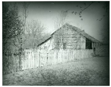 Gottfried Aegerter's first home in West Virginia.  A wooden house stands behind a wooden picket fence, and is surrounded by lots of trees.
