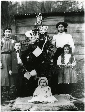 Children stand next to a Christmas tree.