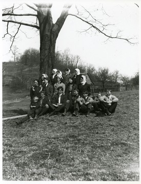 A group boys are sitting while a group of young ladies are standing in front of a tree in Helvetia, West Virginia.