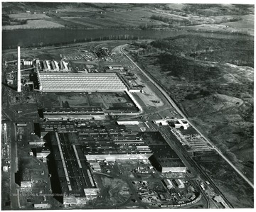 'An overall aerial view of Kaiser Aluminum's Ravenswood Works located on the Great Bend of the Ohio River, six miles south of Ravenswood and midway between Pittsburgh and Cincinnati.  Fabrication Plant is shown in the foreground, casting facility in the center and the Reduction Plant in the background near the 613 foot chimney.  On the main line of the B and O Railroad and West Virginia State Route 2, the Works is two days' delivery time from 50 of the nation's 100 largest cities and 70 percent of the aluminum consuming market.  Public Relations Dept.  Ravenswood Works.  Kaiser Aluminum and Chemical Corp. Ravenswood, W. Va.'