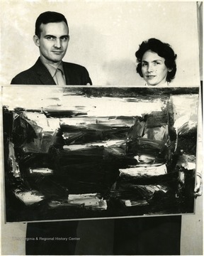 A man and woman hold an abstract painting.