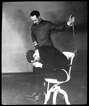 World War I Lantern Slide Show.  Slide No. 03 in group of originally numbered slides.  Physical examination of a recruit sitting in a chair.  This is apparently a balance test for a potential pilot.  Frame is labelled with text saying 'Visual Bureau, University of Pittsburgh.'  (negative no. 3-8246 is inscribed on slide)<br /><br />
