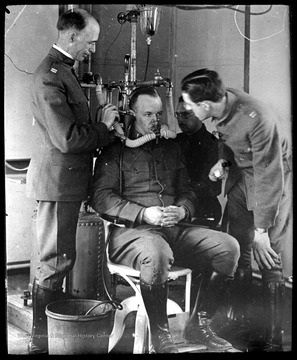 World War I Lantern Slide Show. Slide No. 06 in group of originally numbered slides. Physical examination of a recruit sitting in a chair breathing into a mask.  This is apparently a respiration test for a potential pilot. Frame is labelled with text saying 'Visual Bureau, University of Pittsburgh.'  (negative no. 6-19353 is inscribed on slide)