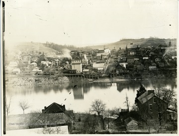 'View of Morgantown taken from the west side, showing old brick house on the west side, Business district at the Wharf. Shows the old firehouse at the Decker's Creek end of Walnut Street, and the old Academy tower on the left. Note the smoke at the mill at the end of Wharf Street.'
