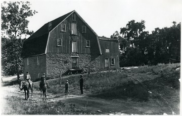 View of a large stone barn building next to a road and men on horseback at Ft. Spring.