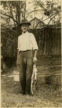 A photograph of Isaac Newton Ballard after he had gone fishing. You can see a pole in one hand and fish in the other.