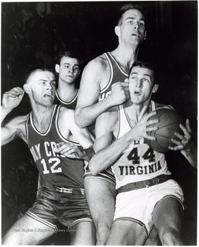 Jerry West is fouled by Ralph Brandt in attempting a lay- up against Holy Cross. Number 12 is George Blaney.