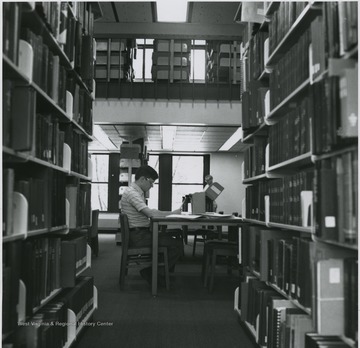 Student looking at manuscript materials and man standing in background.