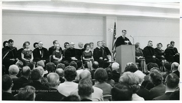 'Dr. Harry Heflin, acting president at podium, and various faculty members' including Dr. Wes Bagby seated at far right, Stillwell seated third from right, and Ruel Foster seated at far left.