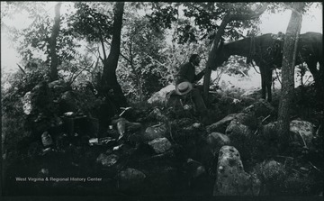 A photograph of a group of people eating a meal on rocks in a wooded area with a horse in the background. '181.D(107); Aug. 8 Fri. 1:35 pm'