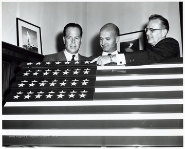 A photograph of Senator John D. Hoblitzell, Jr. (center) and Kaiser Aluminum officials presenting a flag made with aluminum manufactured at Kaiser's Ravenswood, W. Va. plant. At the time of event Senator Hoblitzell lived in Ravenswood.