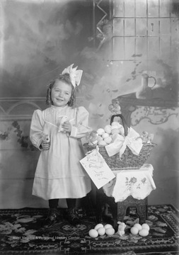Little girl poses with her stuffed animal bunny next to a basket of Easter eggs.